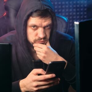 A man in a black hoodie contemplating while using a smartphone, surrounded by digital screens.